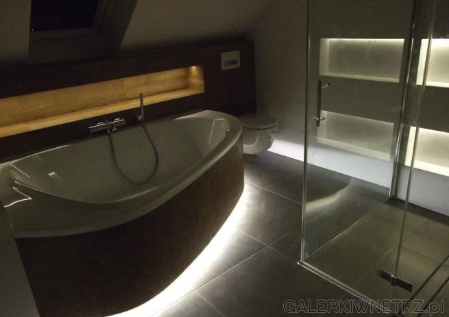 Elegancki projekt łazienki z asymetryczną białą wanną, od zewnątrz zabudowaną brązową ...