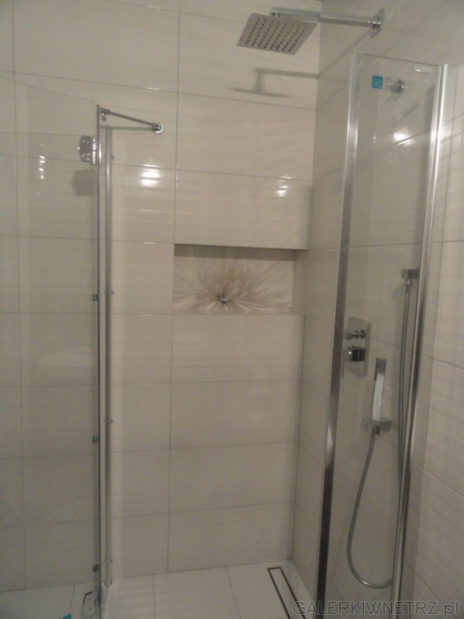 Pod prysznicem ściany wyłożone są aż do sufitu białą glazurą, lekko przełamaną ...